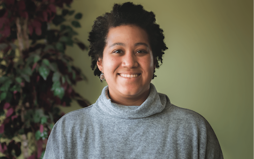 Photo of Erin Royals smiling at the camera. She is wearing a grey sweater.